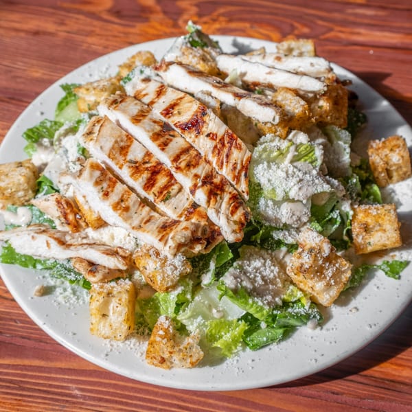 Grilled chicken Caesar salad with croutons and parmesan cheese on a white plate.