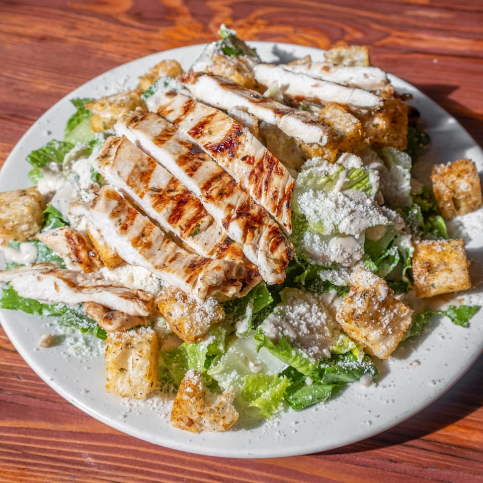 Grilled chicken Caesar salad with croutons and parmesan cheese on a white plate.