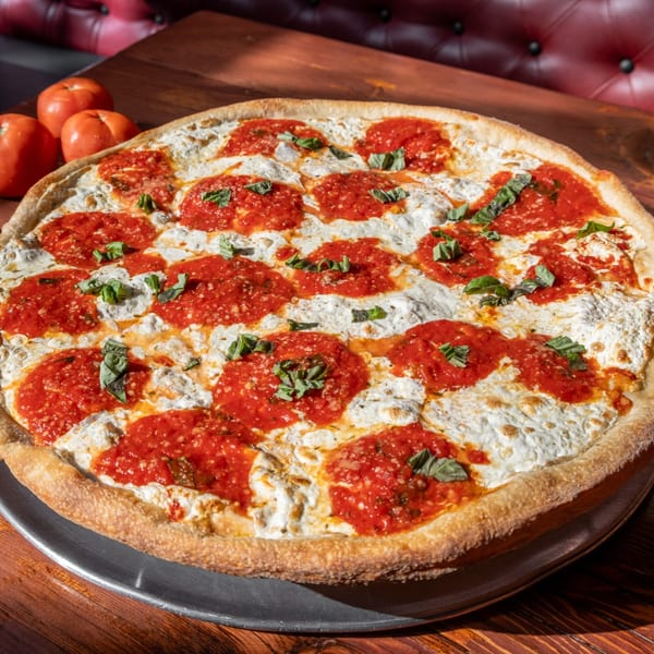 A large white pizza with dollops of red sauce and fresh basil on a metal pan.