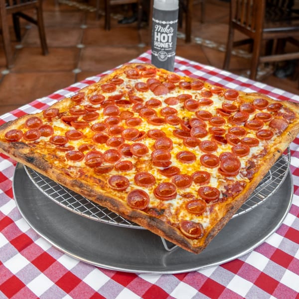 Square pepperoni pizza on a wire rack, with Mike's Hot Honey bottle on a red and white checkered tablecloth.