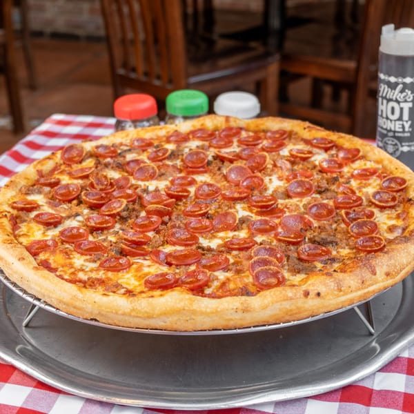 A pepperoni and sausage pizza on a metal stand, with hot honey and shakers in the background.