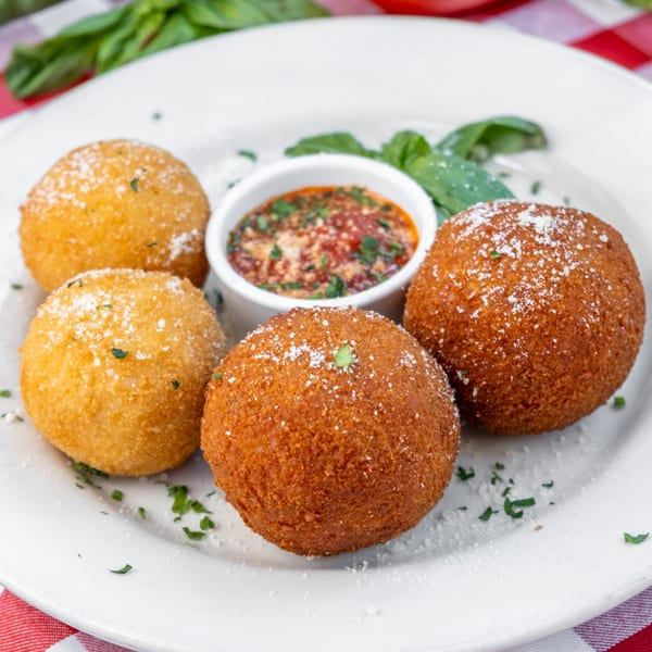 Four golden-brown arancini balls with a side of marinara sauce, garnished with parsley and basil.