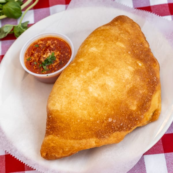 Golden-brown calzone with a side of marinara sauce, garnished with parsley, on a white plate.