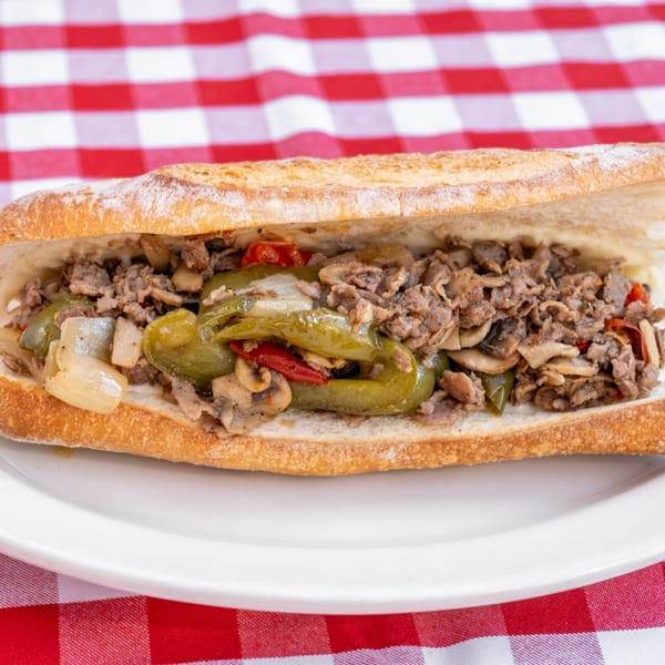 A steak and cheese sub with peppers, onions, and mushrooms on a white plate.